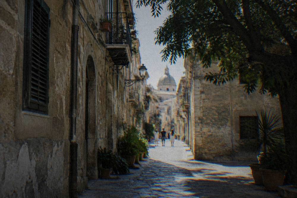 A narrow old Sicilian street with worn stone buildings in soft light