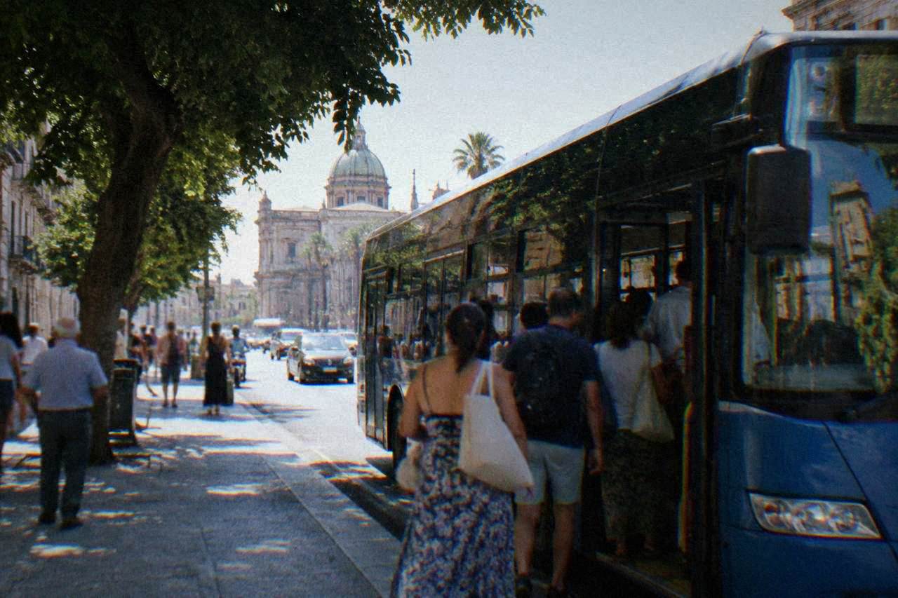A city bus stopped at a busy street in central Palermo with passengers boarding