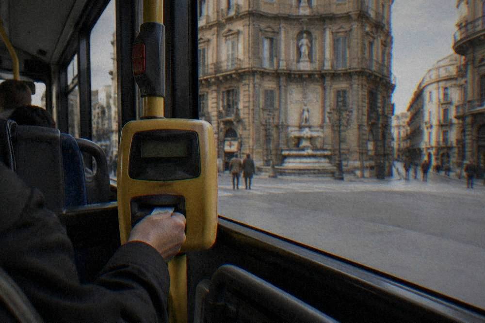 A passenger inserting a paper ticket into the validation machine inside a Palermo bus