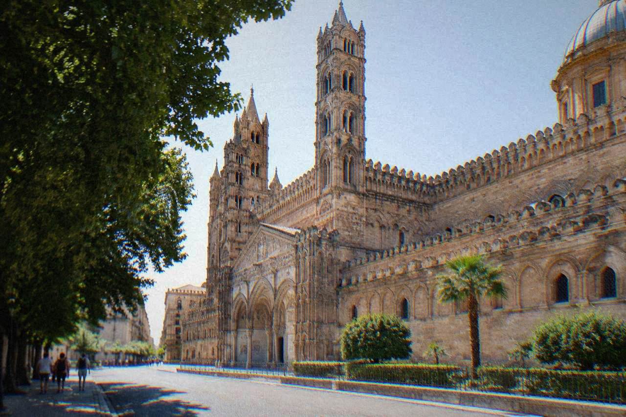 The western front of Palermo Cathedral seen from the street, with its towers and arcaded wall in warm stone