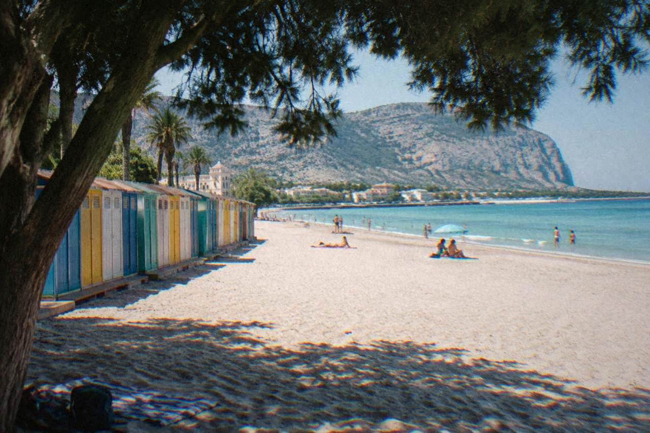 A wide sandy beach with calm turquoise water and a line of colourful changing cabins behind the sand
