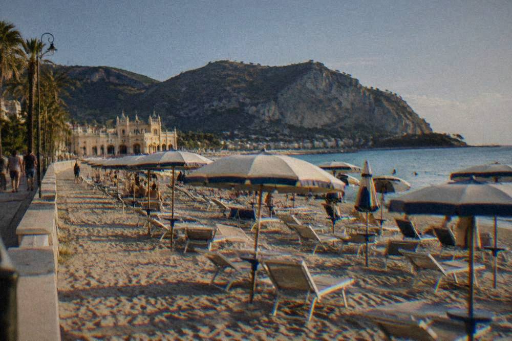 Rows of umbrellas and sunbeds on a sandy beach in front of a seaside promenade