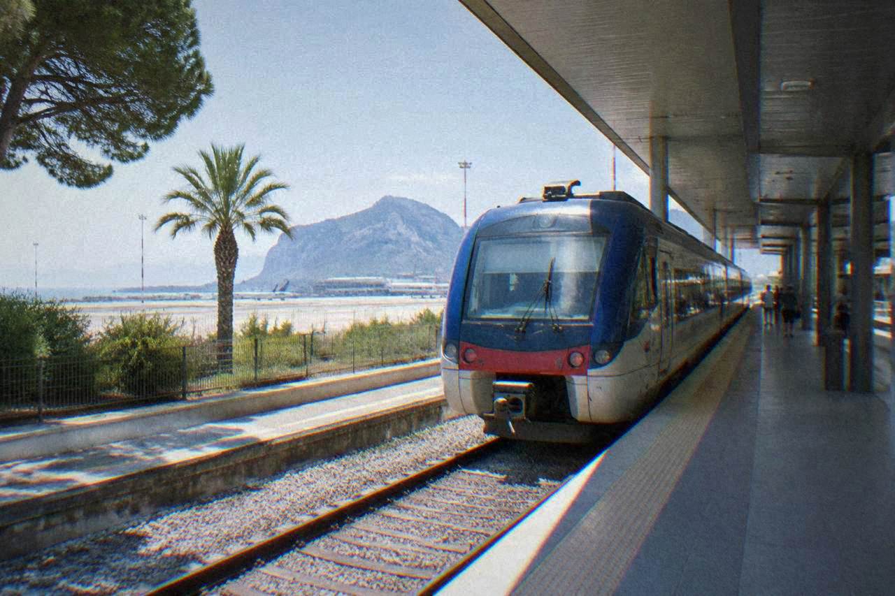 A regional train waiting at a platform inside a modern airport railway station in Sicily