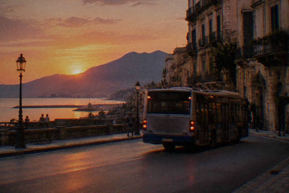 A city bus passing along a Palermo street lined with old buildings in warm evening light