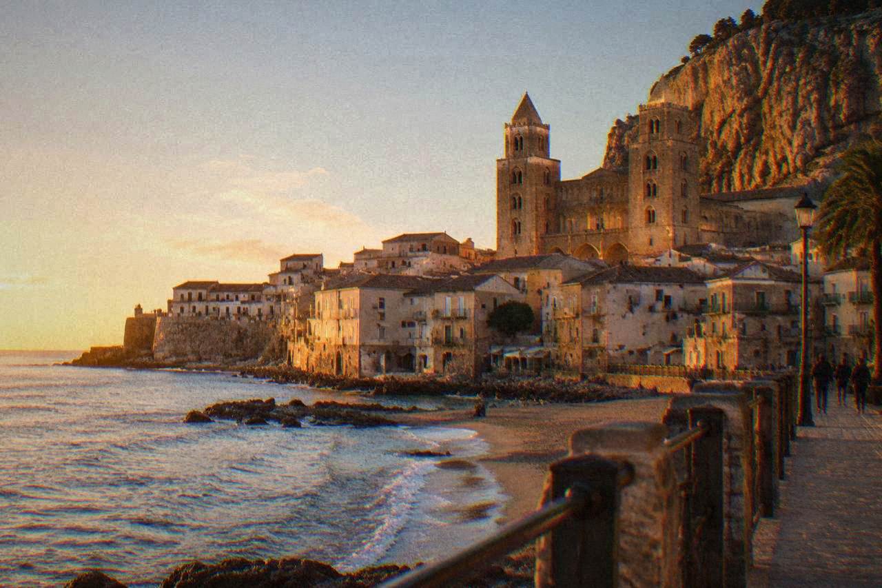 The seafront promenade of Cefalu with the town's buildings rising toward the rocky headland