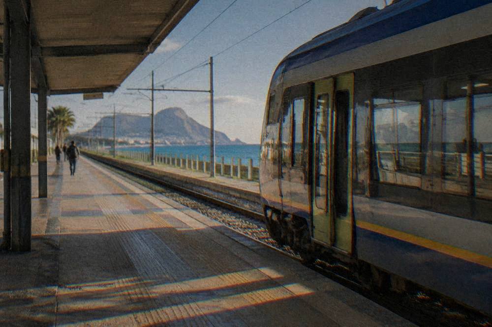 A regional train standing at a small coastal station with the sea visible beyond the platform