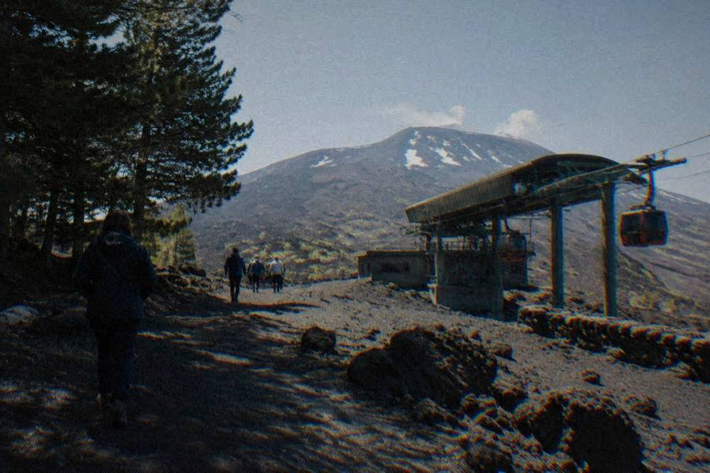 Visitors in jackets walking on dark volcanic rock near an Etna cable car station