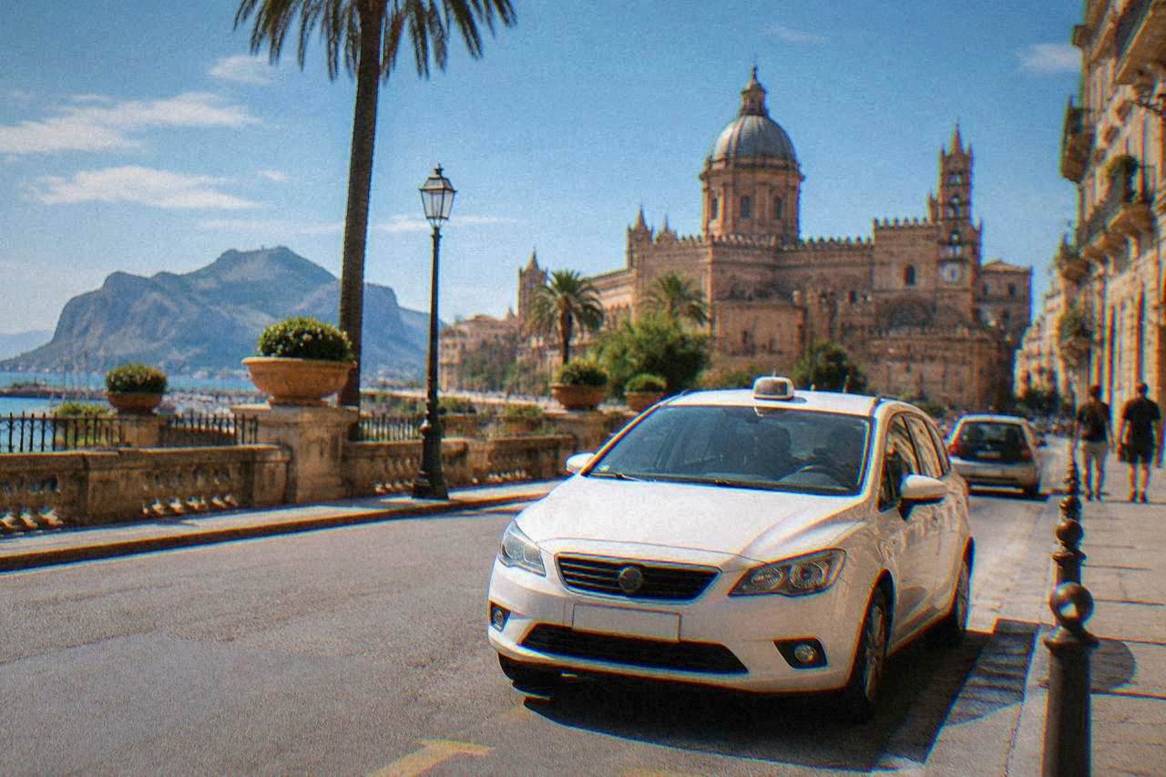 A white licensed taxi waiting at a rank on a sunlit Palermo street