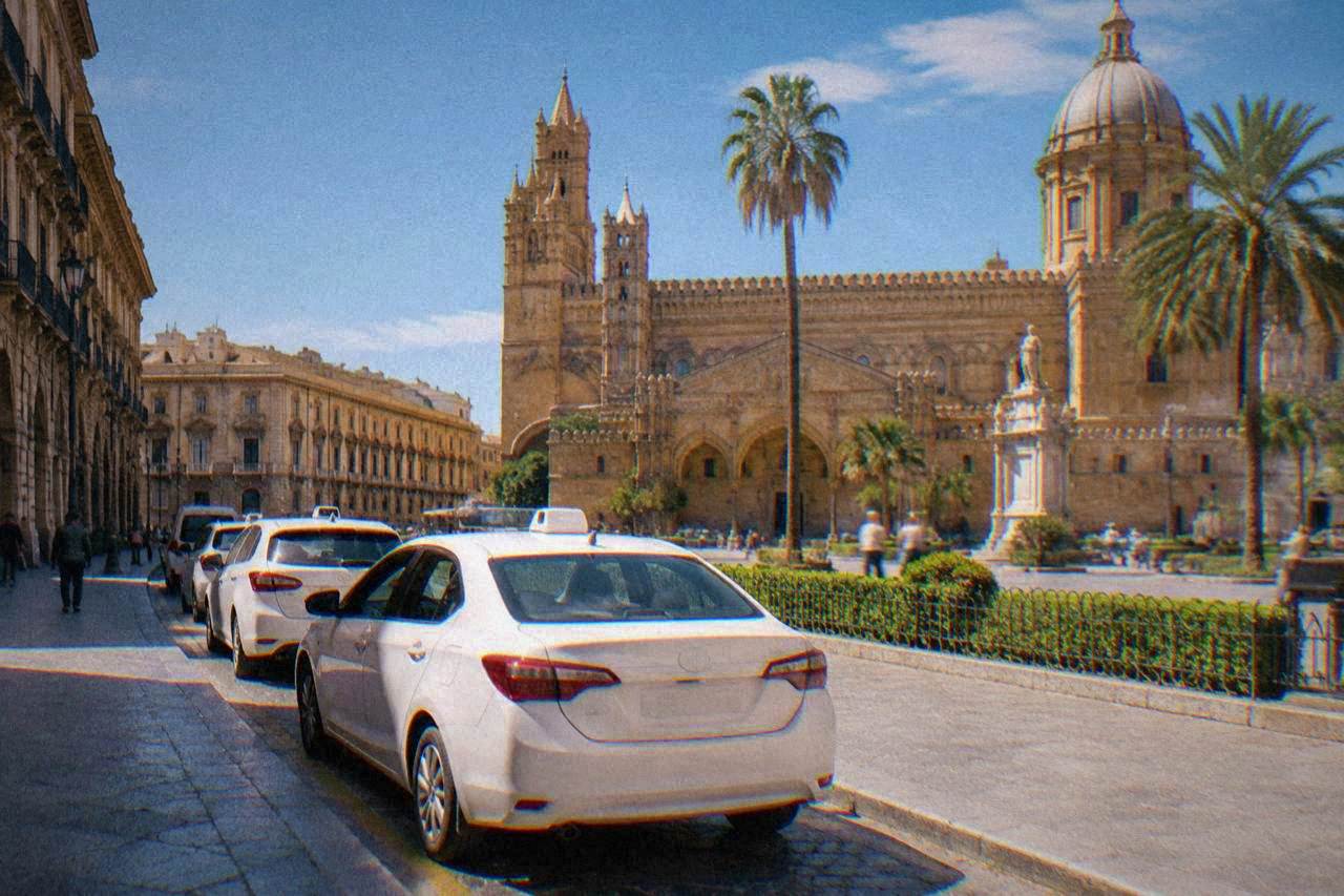 A white taxi waiting in a line at a rank beside a sunlit Palermo piazza