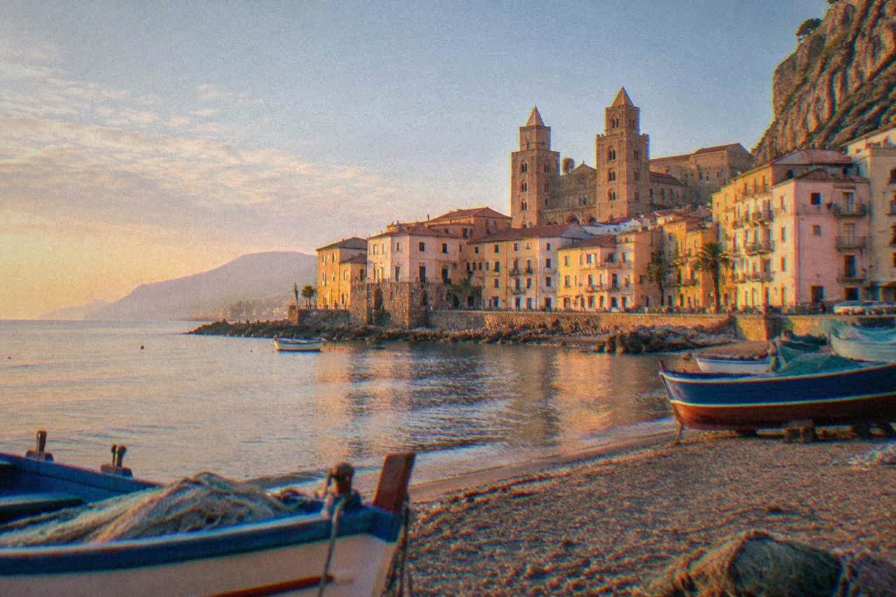 Fishing boats and pastel houses along the seafront of Cefalù at golden hour