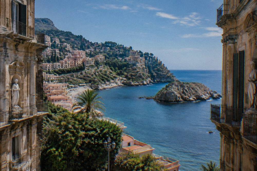 Coastal hillside town with terraced buildings above a sheltered bay and rocky islet
