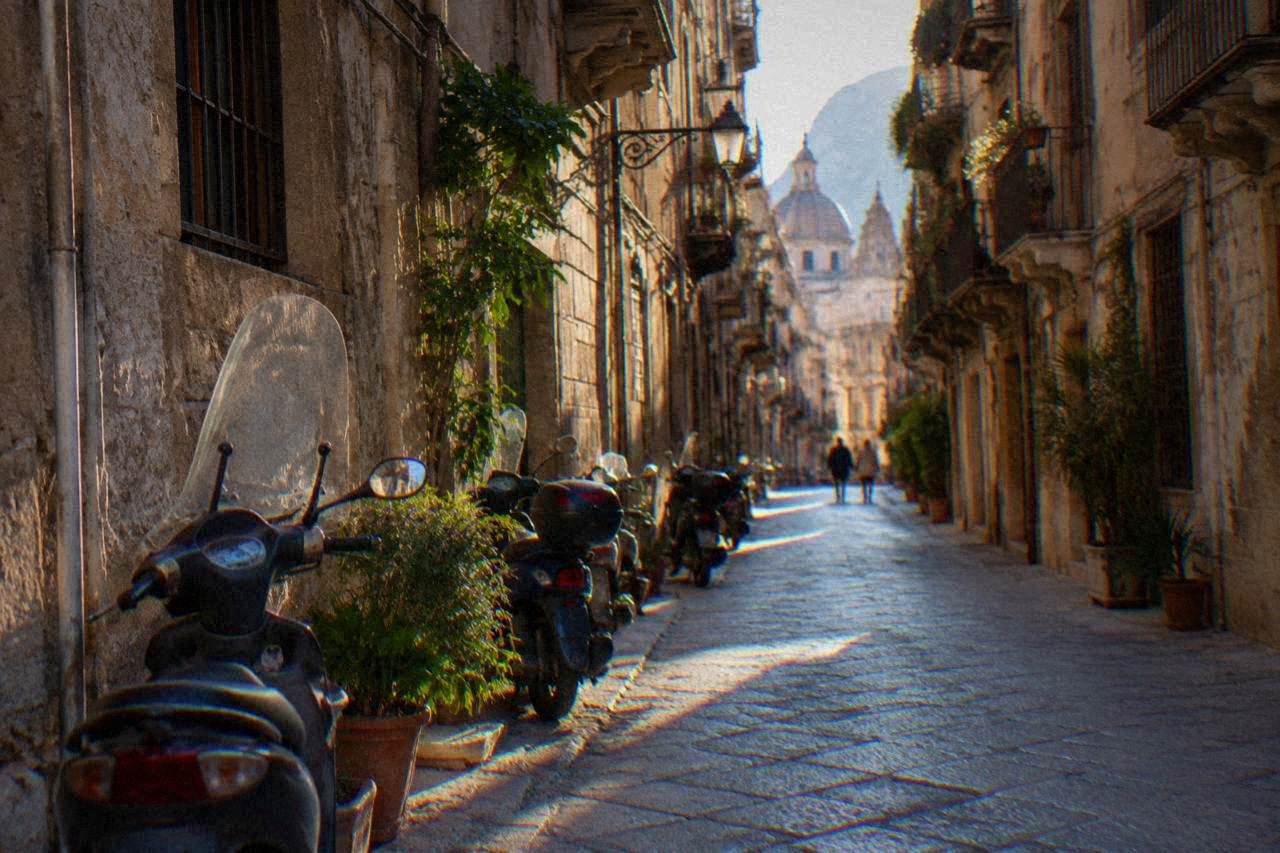 A narrow street in the historic centre of Palermo with parked scooters and old stone buildings