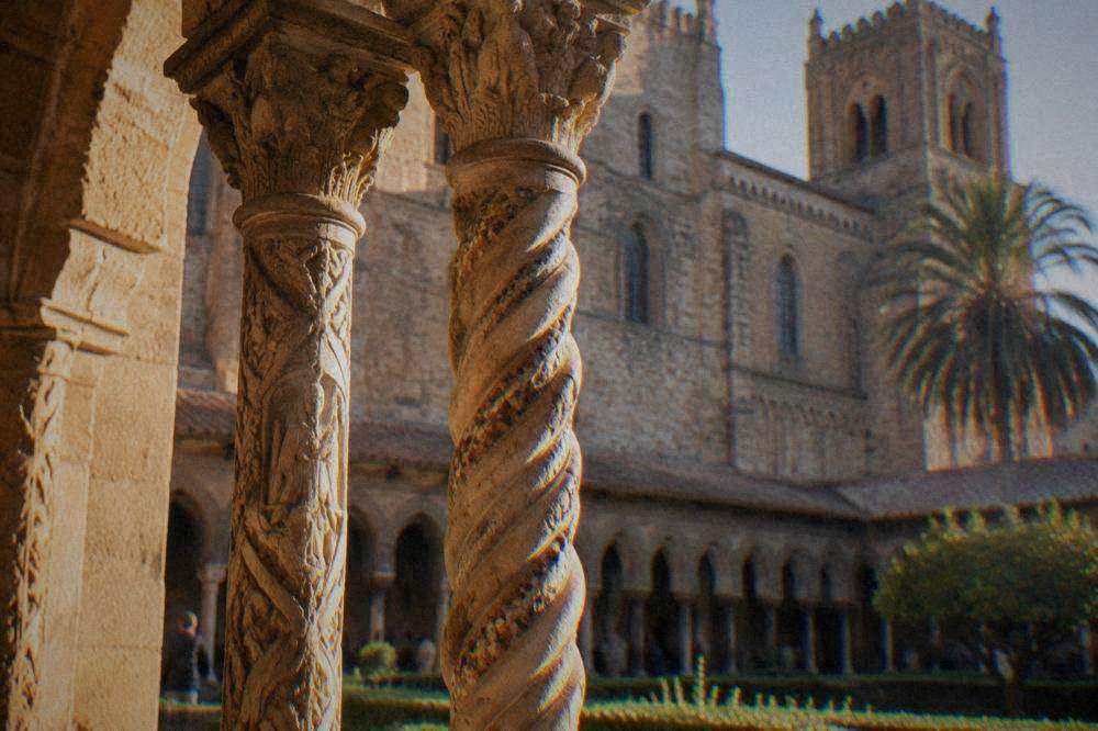 Carved twin columns of the Monreale cloister under sunlight with the cathedral wall behind