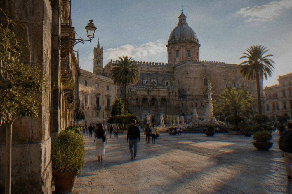 A Palermo square with historic buildings and people walking in late afternoon light