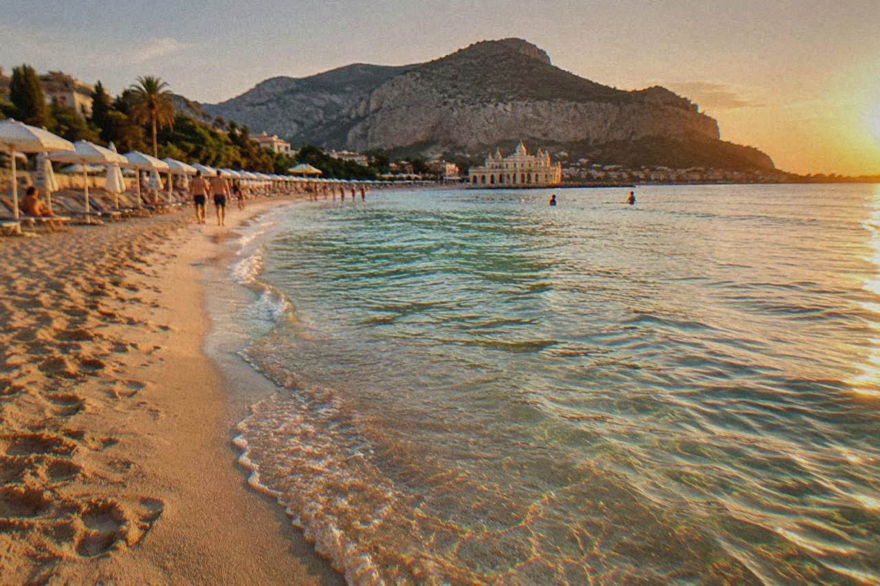A wide sandy beach with clear shallow water and a line of umbrellas along the shore