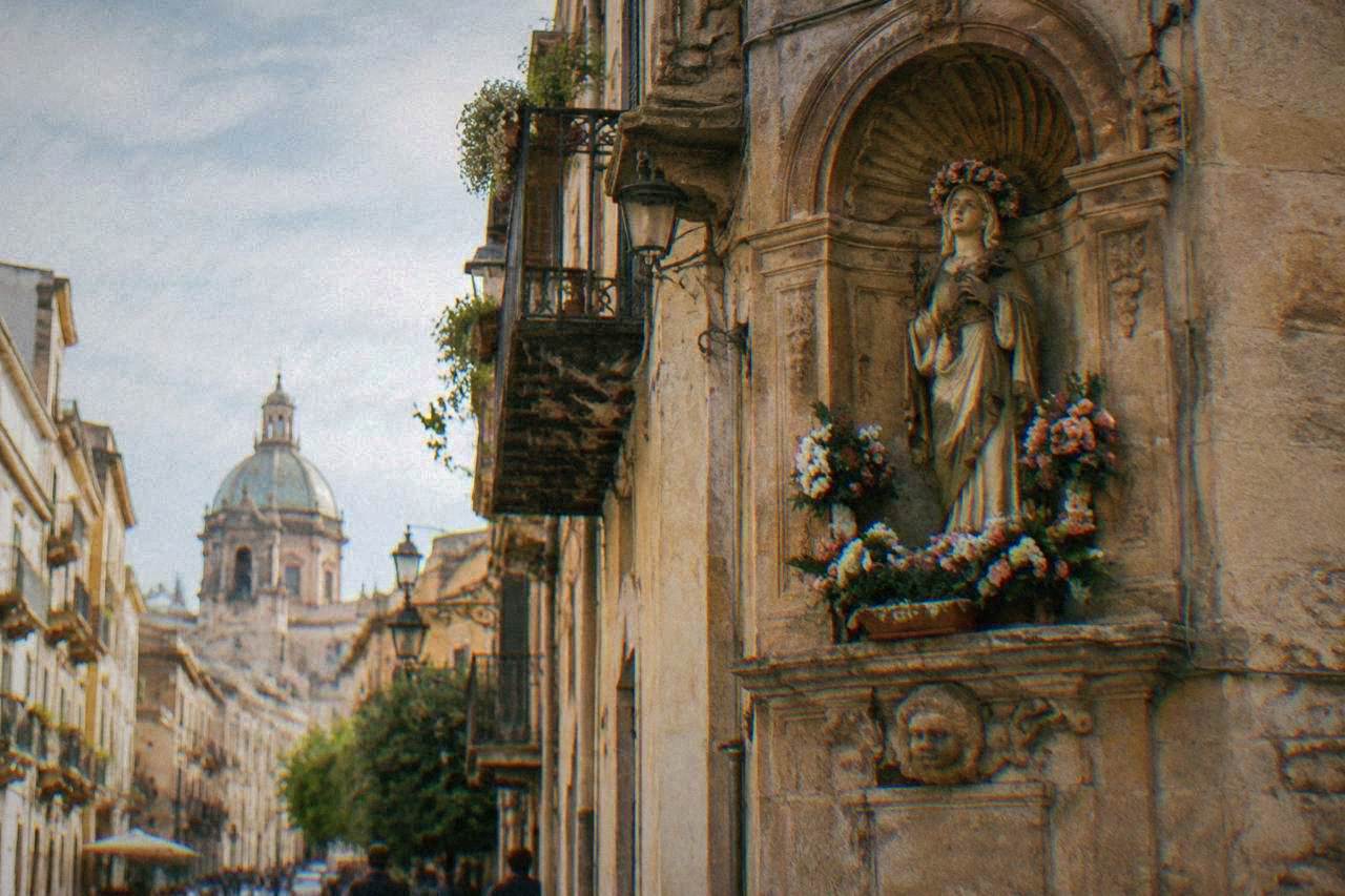 A statue of Saint Rosalia in a niche above a Palermo street, decorated with flowers