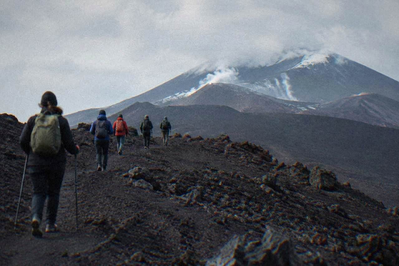 A guided group walking across dark volcanic rock on the upper slopes of Mount Etna