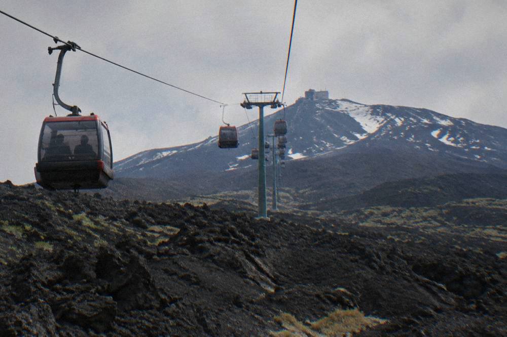 Cable car cabins ascending over black lava fields toward the upper station on Mount Etna