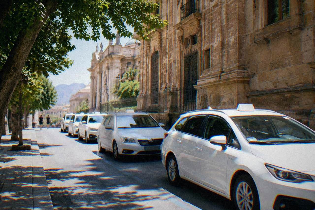 White licensed taxis lined up on a sunny street beside a historic stone building in Palermo