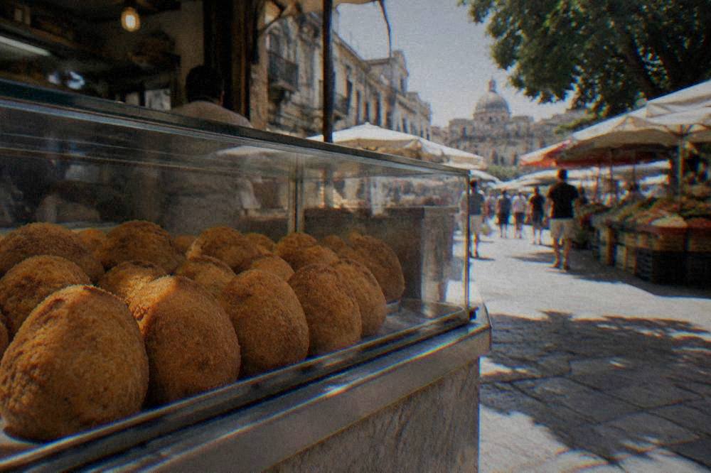 A row of round fried arancine in a glass display case in a Palermo fry shop