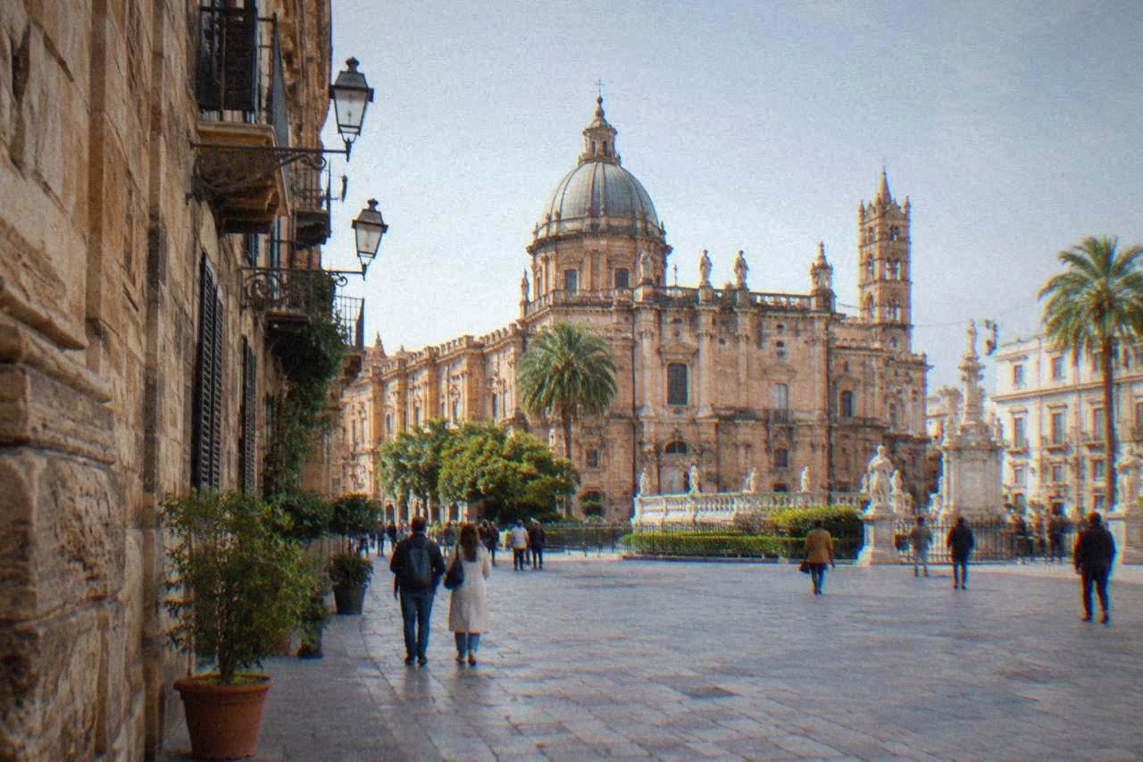 Sunlit square in central Palermo with historic facades and people walking under a clear sky