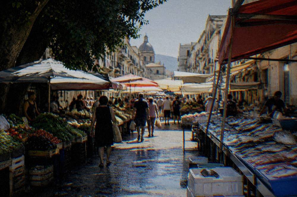 A busy Palermo market lane with stalls of vegetables and fish and shoppers moving between them in morning light