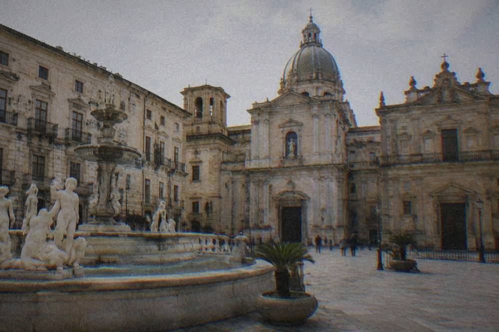 A restored Palermo piazza with a fountain and church facades under a bright sky