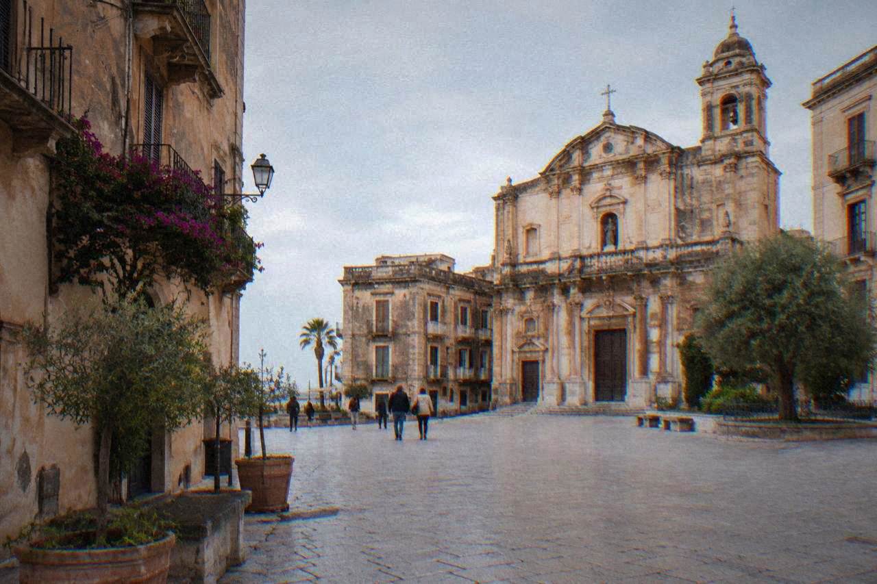 A sunlit square in the Kalsa district of Palermo with old stone buildings and a church facade