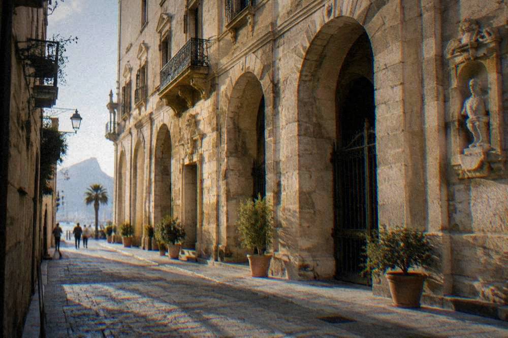 The arched stone facade of a historic palace on a narrow street