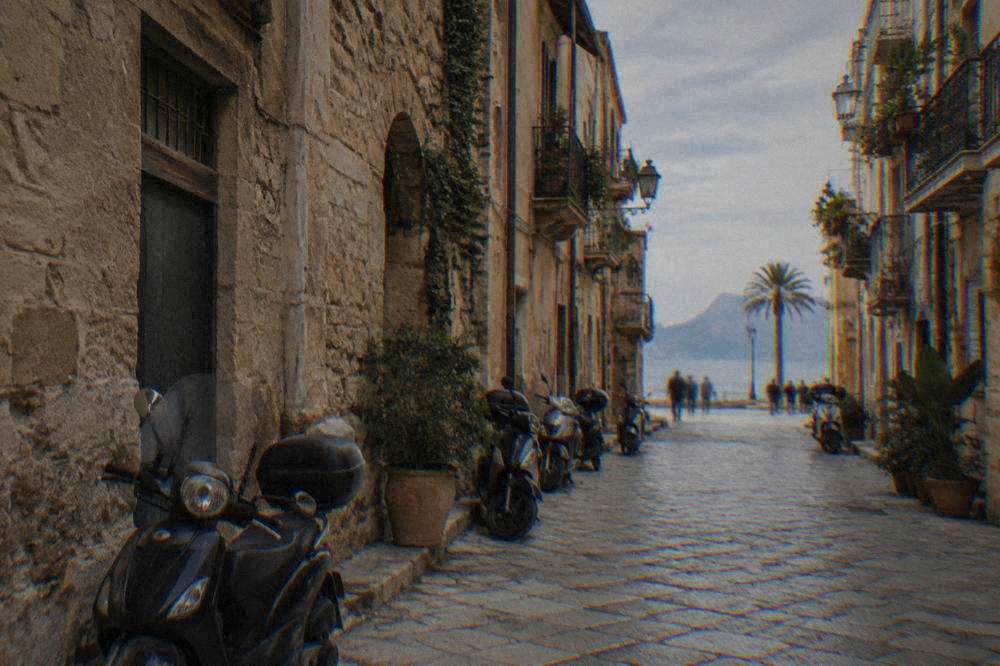 A narrow Kalsa street with stone paving and parked scooters