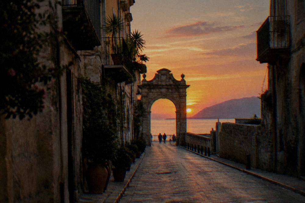A view along a straight old street toward a sea gate at sunset