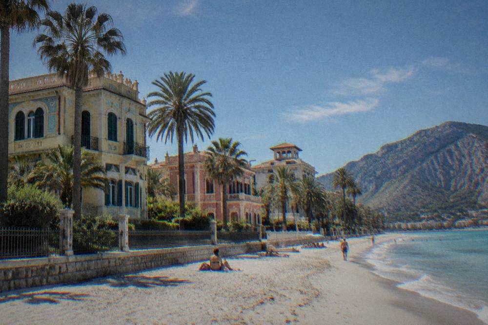 Colourful Liberty-style villas with decorative facades behind palm trees in a seaside street