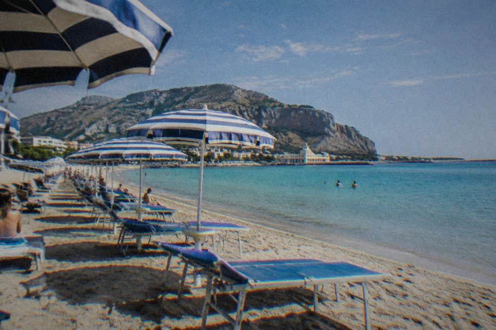 Rows of sunbeds and striped umbrellas on sand beside calm turquoise water