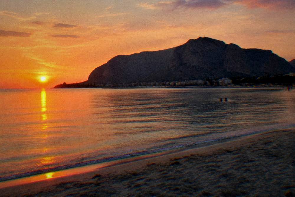 Sunset light over a calm bay with a sandy shore and distant mountain headland