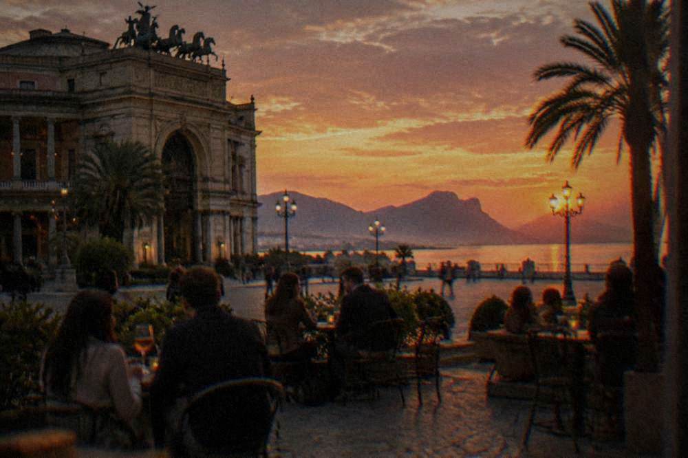 People eating and drinking at small tables outside an evening bar in a city square