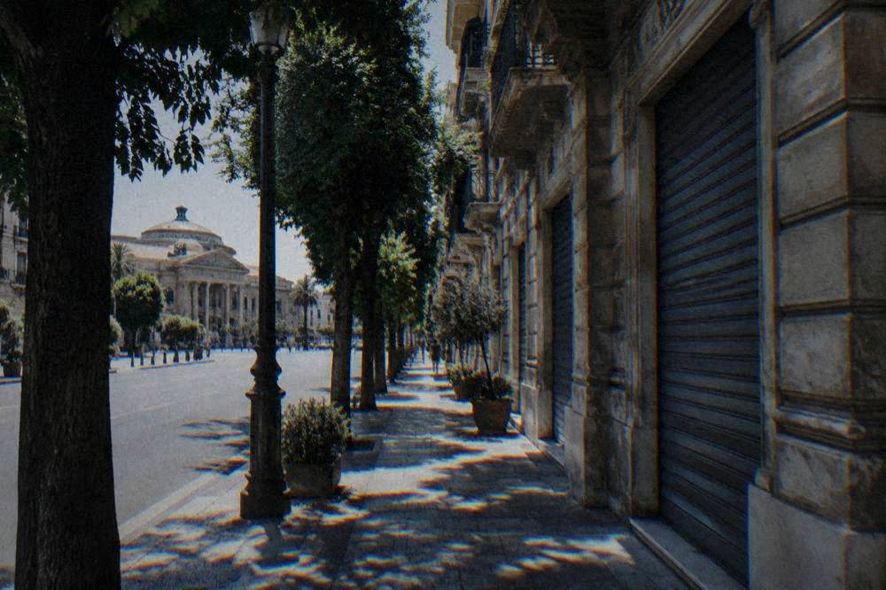 A calm morning street of closed shutters and stone facades in a Sicilian neighbourhood