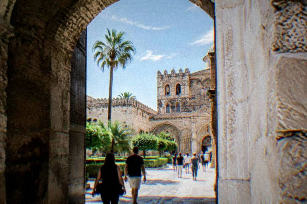 Visitors walking through a stone archway into the Palazzo dei Normanni complex