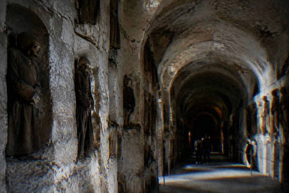 A dim vaulted stone passage with arched recesses receding into darkness