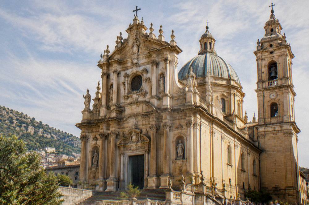 A hill town cathedral with a decorated facade under a bright sky