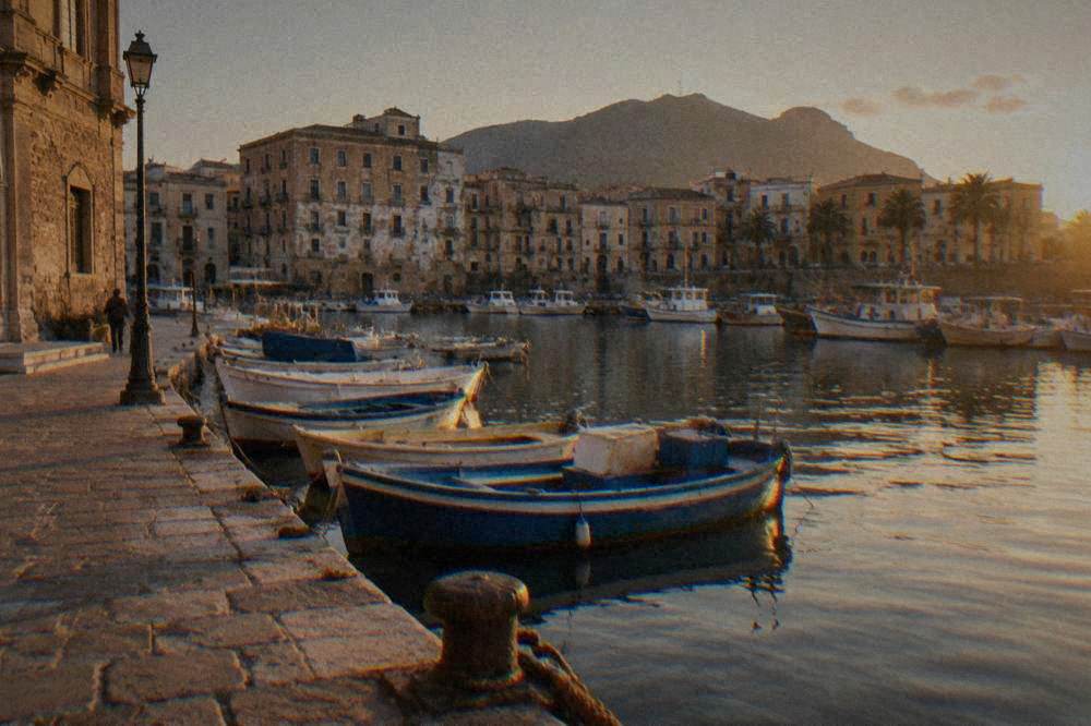 A historic marina with small moored boats framed by old stone buildings in Palermo