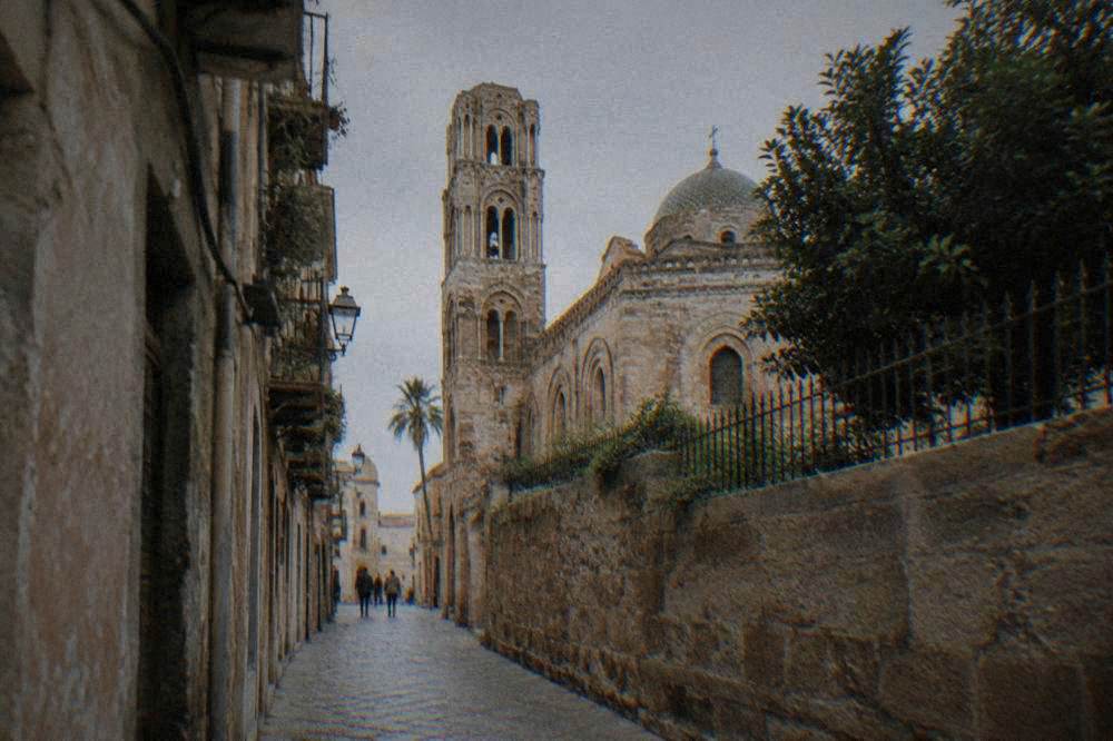 Narrow old street with worn stone buildings leading toward a church tower