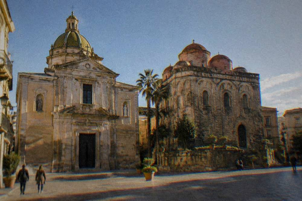 Two church facades side by side with domes above a sunlit square