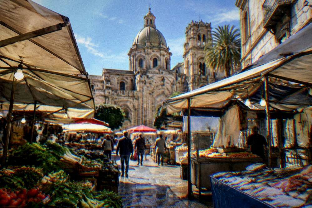 Busy market street with stalls of vegetables, fish and fried food under awnings