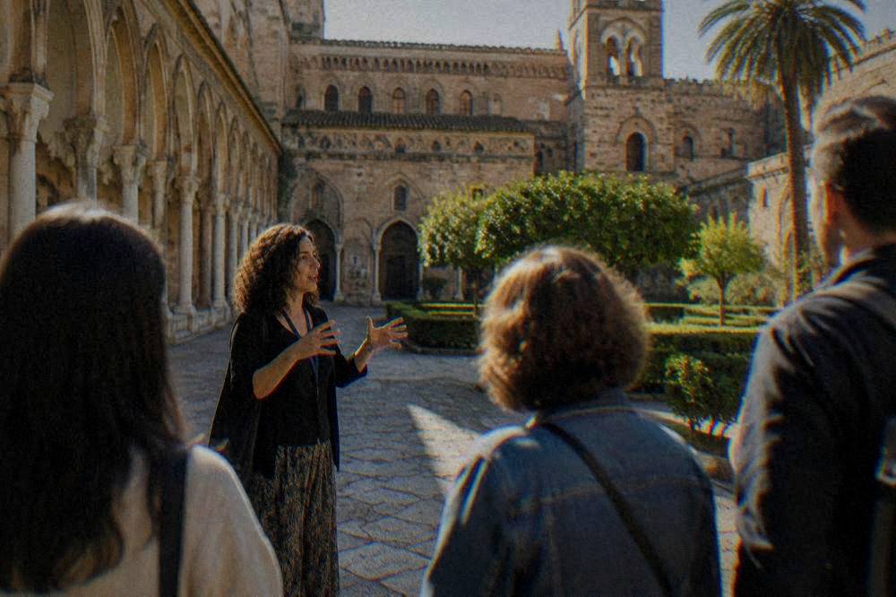 A guide speaking to a small group of visitors in a palace courtyard in Palermo