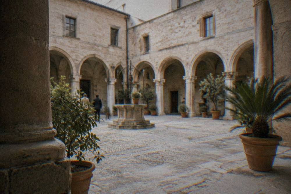 An inner courtyard with arched stone openings and potted plants at a Palermo palace museum