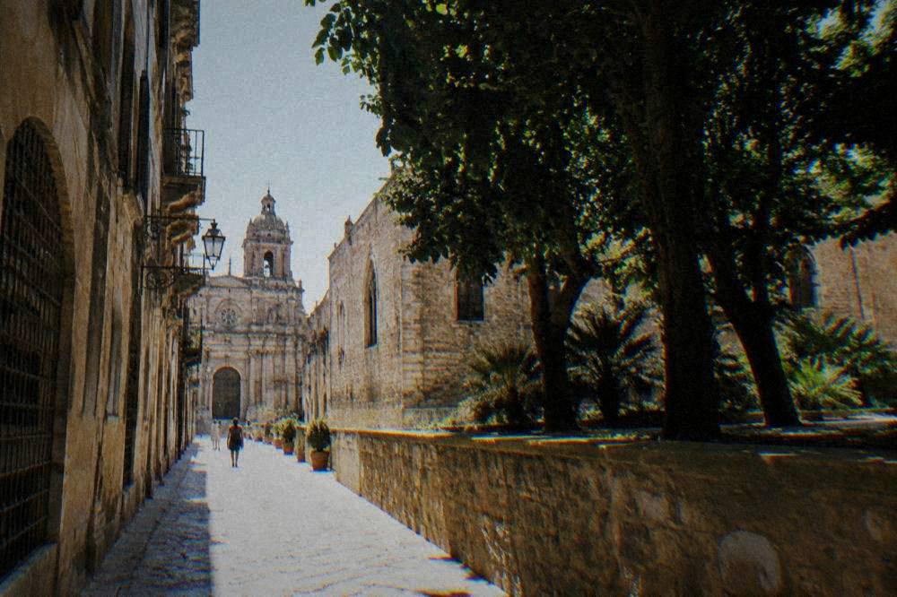A narrow old street with warm stone buildings and a distant church facade in Palermo