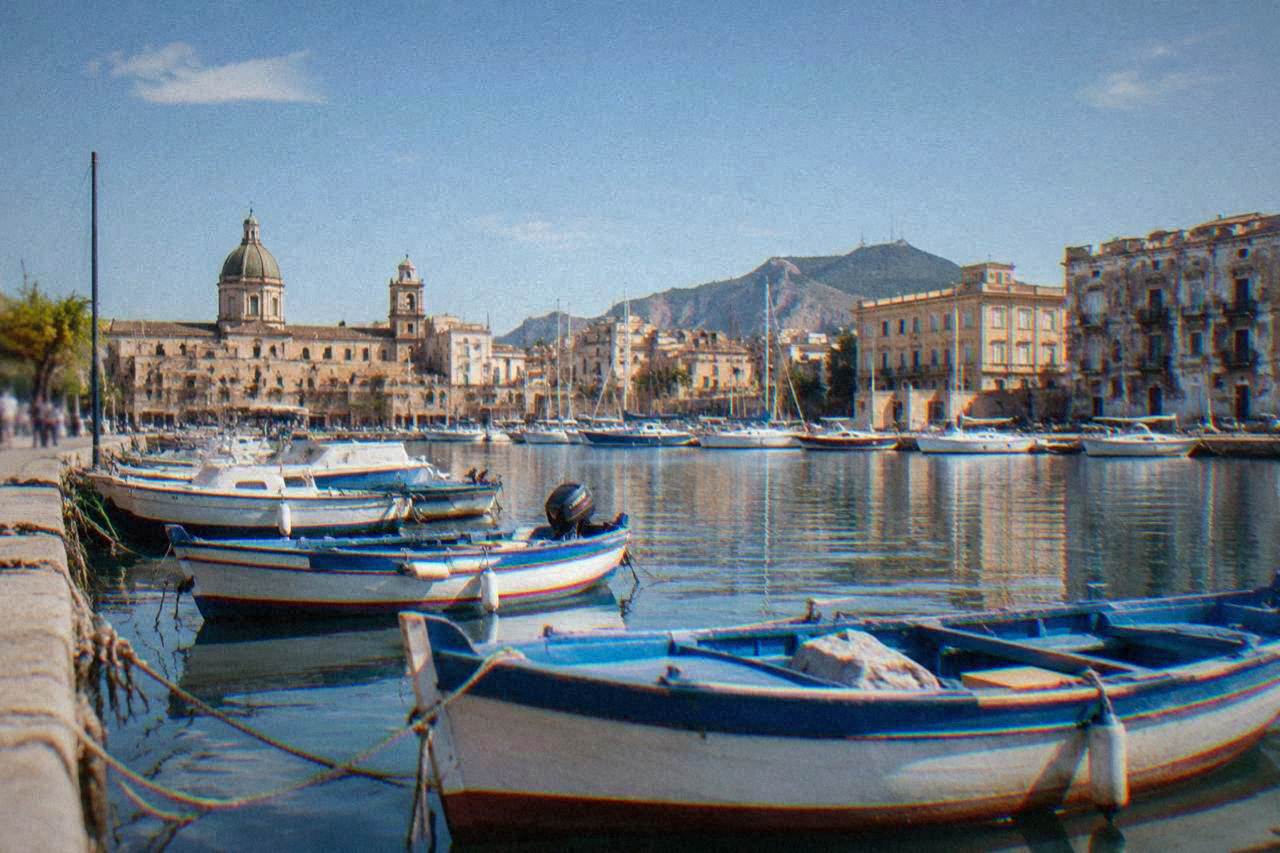 Small boats moored in the historic La Cala harbour of Palermo with old buildings behind them