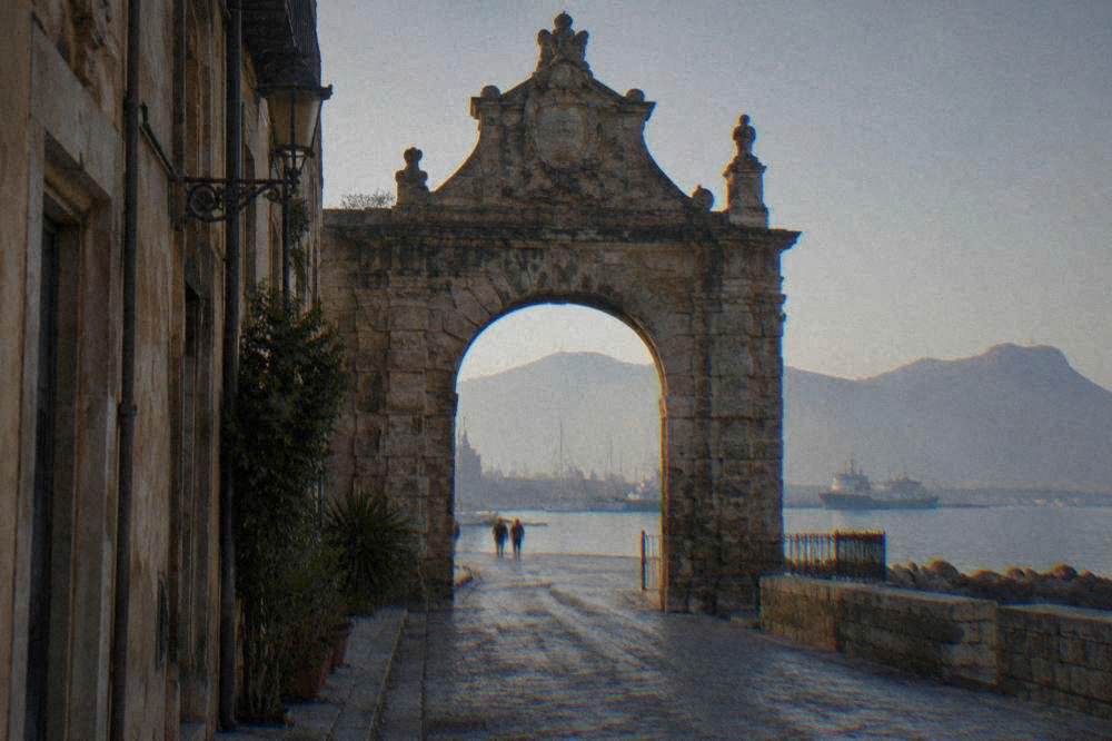 A stone city gate at the sea end of an old Palermo street near the harbour