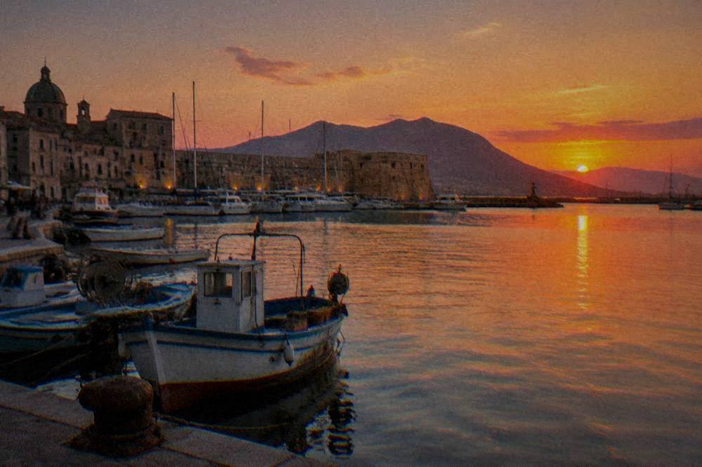 Sunset light over moored boats and old harbour walls in Palermo
