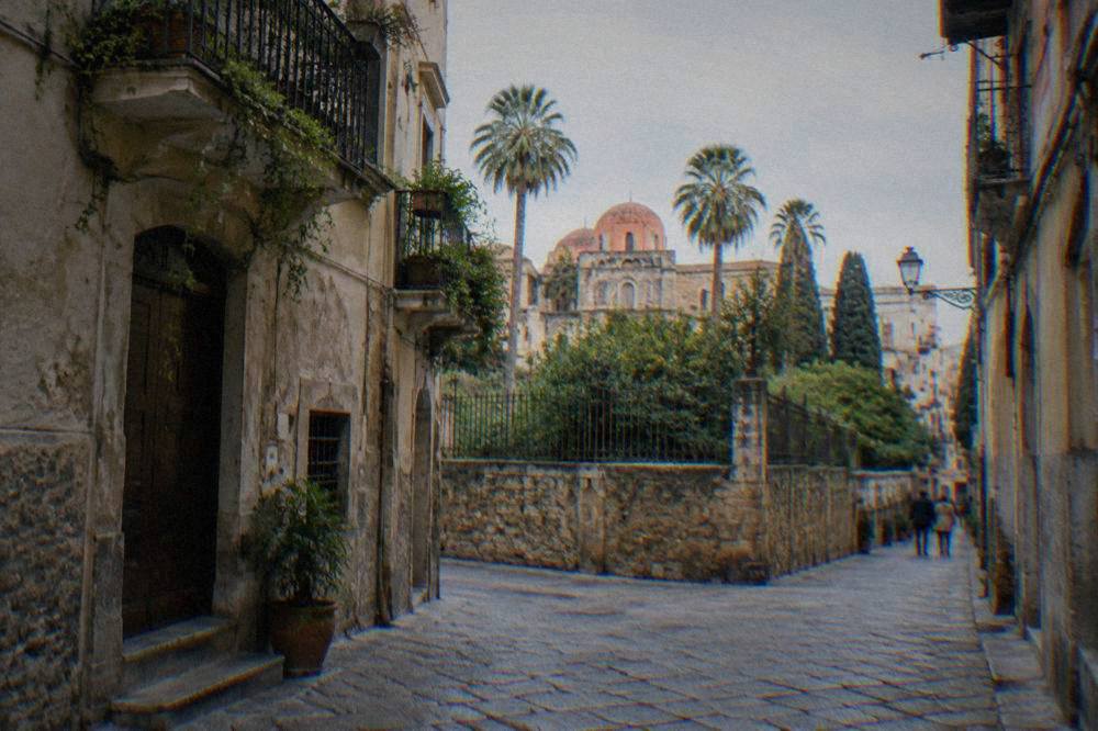 A narrow old street in the Albergheria district leading toward a walled garden in Palermo